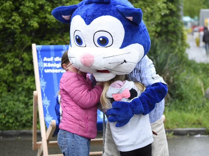 Bild von einem Maskottchen, das am Schwingfest zwei Kinder umarmt.