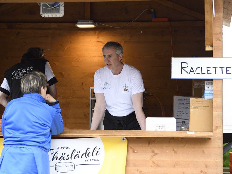 Ein Mann steht in eine Raclette-Stand und spricht mit einer Kundin.